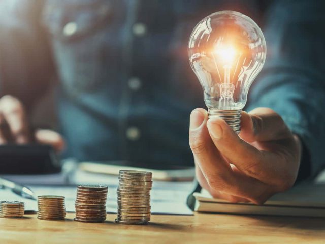 Business,Man,Hand,Holding,Lightbulb,With,Using,Calculator,To,Calculate